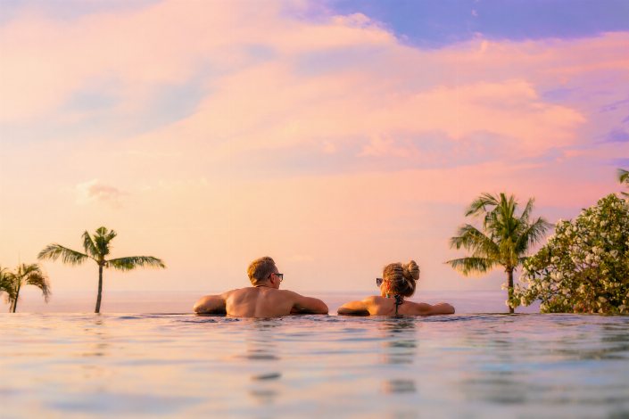 Couple relaxing in an infinity pool overlooking the ocean at sunset.